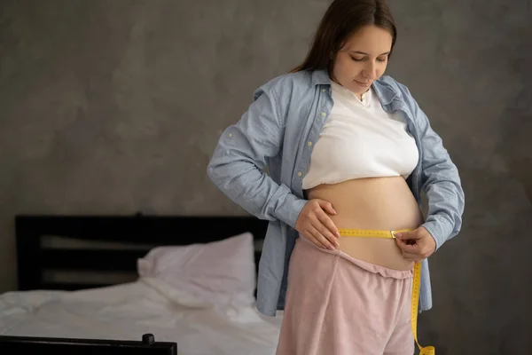 Pregnant Woman Measuring Her Belly While Standing Grey Background Home — Stok fotoğraf