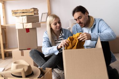 Taşındığı gün bir erkek ve bir kadın yere oturup eşyaları boşaltıyorlar. Yeni bir dairede mutlu bir çift. Ev kiralama ve satın alma kavramı. Boşluğu kopyala.