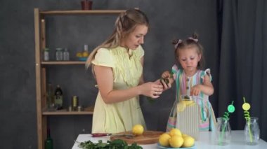 Cute girl and her young mother cooking in the kitchen and cook freshly made lemon lemonade