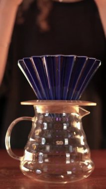 The first stage of brewing filtered coffee. The barista put the brewer sets the coffee filter and pours hot water from a special kettle on it. Close-up, no face. vertical video