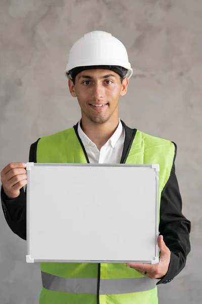 Portrait of arabic engineer with blank space, male architect holding whiteboard for text on gray background, building and renovation concept
