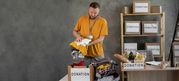 Volunteers collecting food donations in warehouse. volunteer man holding donations boxes in a warehouse, putting clothes in donation boxes, social worker making charity. Banner, empty space