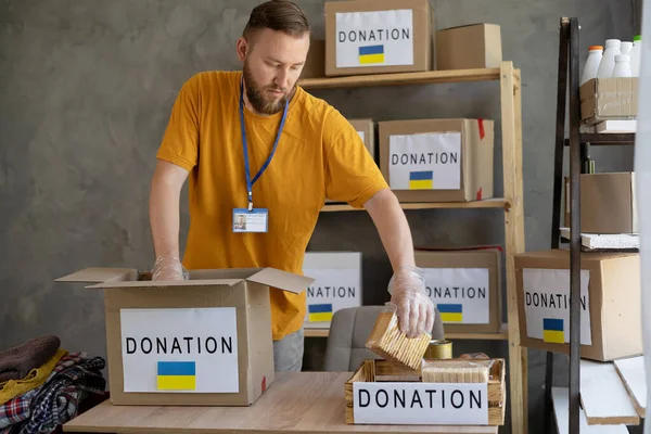 Volunteers collecting food donations in warehouse. Volunteer collect donations for Ukrainian refugees, humanitarian aid concept.