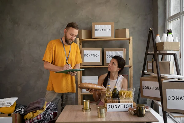 Volunteers collect donations for food at the warehouse. A team of volunteers keeps donation boxes in a large warehouse. social worker taking charity notes. Donation Concept.
