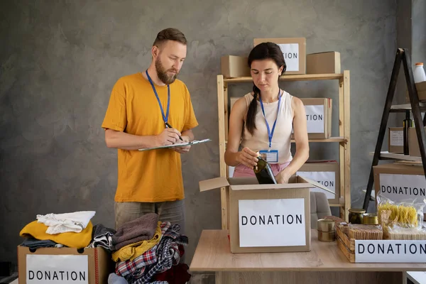 Helpful team of social workers. Young people volunteering to sort donations for charity food drive. Cardboard boxes being filled with food donations. social worker taking charity notes. Donation Concept.