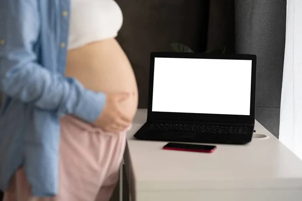 Online consultation. Pregnant woman talking with doctor via video call standing with laptop at home.