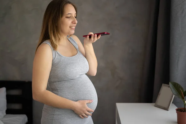 Happy young mom send voice message record audio blog on cell devoted to anticipation parenthood maternity. Positive mother dictate vocal letter to beloved child. pregnancy and technology concept