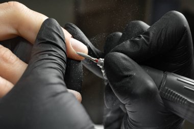 Close-up of manicurist uses an electric drill to remove old gel polish from nails. A woman is getting a manicure of nails. The beautician files the client's nails. professional manicure tool.