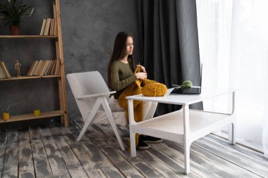 Woman is learning to knit on video lessons from the Internet, development of new skills, knitting, girl knits while and watching movie on a laptop, hobbies