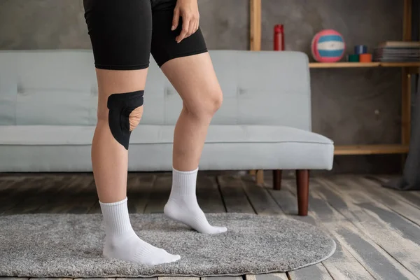 Female knees with physio tape on knee at home. Physiotherapy concept.