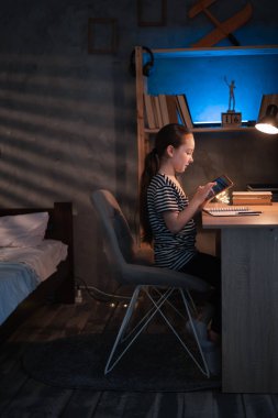 Schoolgirl doing her homework with digital tablet at home in the evening. Child using gadgets to study. Children, education and distance learning concept