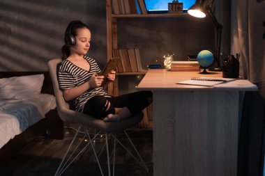 Caucasian pupil watching something on tablet computer at night, portrait of preteen girl in wireless headphones using digital tablet at home