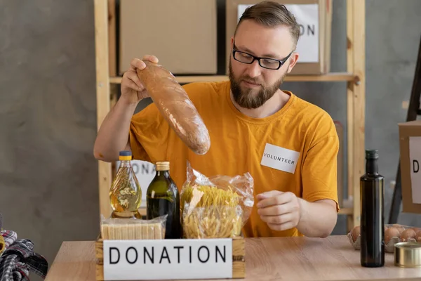 working for a charitable foundation. Happy volunteer collecting donation box in the office. Volunteer sorting donations. male volunteer shares donations. charity, donation and volunteering concept.