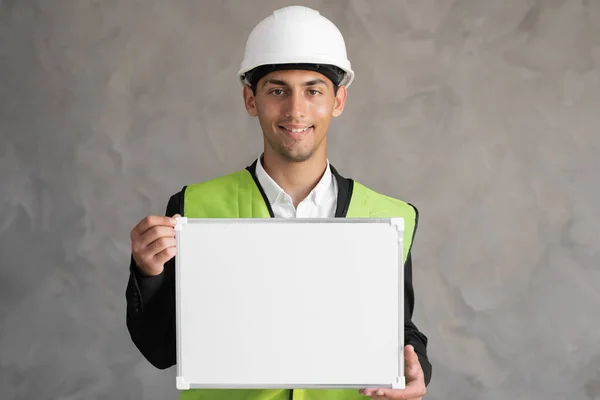 Portrait of arabic engineer with blank space, male architect holding whiteboard for text on gray background, building and renovation
