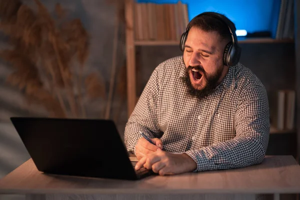 Indian tired man with laptop working at night office and yawning. business, overwork, deadline and people concept