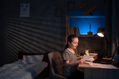 Pretty schoolgirl studying homework math during her online lesson at home at late evening, self-isolation, online education concept, home schooler