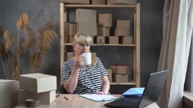 Time for coffee break. Older woman small business owner in casual wear holding a cup of coffee while sitting at her working place in home office. start up and SME concept