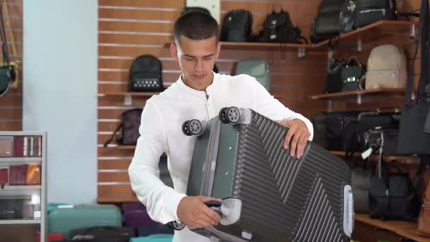 Young Caucasian Man Stands Suitcase Store Chooses Bag His Hand — Vídeos de Stock