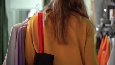 A woman chooses clothes in a womens clothing store. She took several options and goes to the locker room to make a choice. The concept of shopping and consumerism.