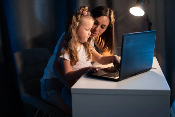 Beautiful mother and child looks at laptop screen using app education program, choose cartoons in the evening, teach kid pc use, controls daughter watching on internet cyberspace concept