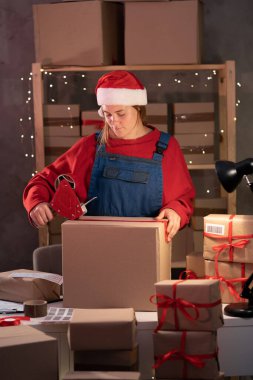 Female entrepreneur small business owner is packing goods at home in a small office. Prepares boxes for shipment. Big sale for Christmas. copy space.