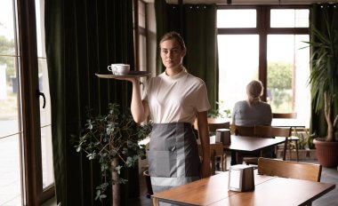 Portrait of cheerful waitress serving on tray cake and cup of beverage in cafe. copy space