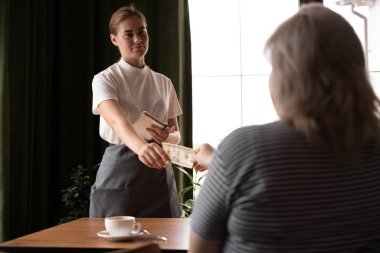 Female client pays in cash in a cafe, woman gives a dollar tip to a waitress, copy space