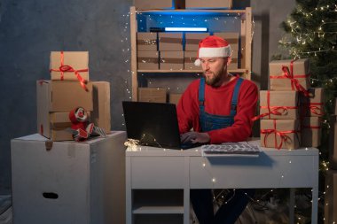 Small business aspiring entrepreneur, SME freelance worker working in a home office man in Santa Claus hat and accepts an online order using an application and a laptop, Christmas sale concept