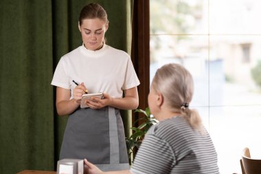 Kafe restoranında müşterilere servis yapan mutlu garson. Misafirlerle konuşan kibar servis elemanı. Yemek ve içecekleri seç, müşteri hizmetleri kavramı.