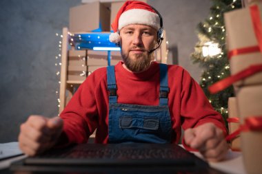 Happy Santa Claus wearing hat using laptop computer sitting at workshop home table late on Christmas eve, webcam view. Ecommerce website xmas time holiday, online shopping e commerce sale