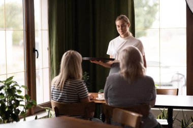 waiter holding aromatic coffee on tray bringing order to cafe guests, coffee shop worker give hot drinks to visitors. Service concept
