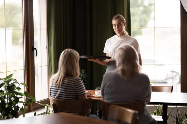 waiter holding aromatic coffee on tray bringing order to cafe guests, coffee shop worker give hot drinks to visitors. Service concept