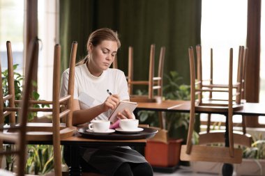 Cafe waiter rests at the end of the working day making notes in a notebook, service concept