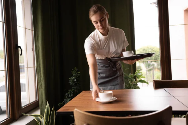 Waiter putting and holding cups on tray working at cafe. Service concept