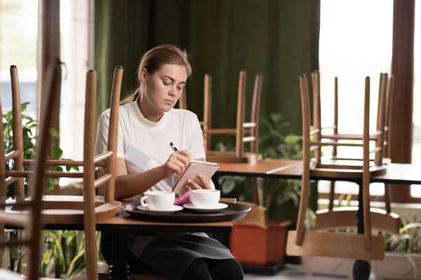 Cafe waiter rests at the end of the working day making notes in a notebook, service concept
