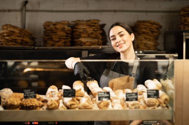 Gorgeous baker woman holding freshly baked bread smiling to the camera happily. Fresh from the oven.