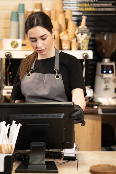 Small startup business owner concept. waitress girl in apron using finger touching screen of POS terminal in coffee shop. young woman staff in coffeehouse take order and print receipt in cafe