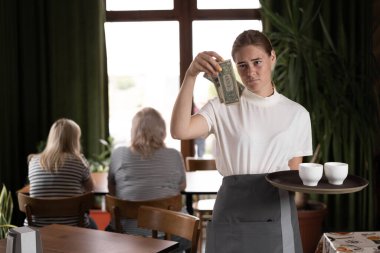 disgruntled female waiter holding serving tray in restaurant with bad tips, copy space