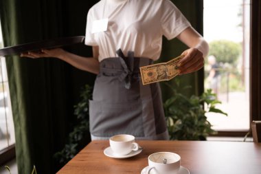 Woman hand taking tip US dollar banknotes from wooden table at cafe. Concepts for payment, service charge, bill checking, money tips.