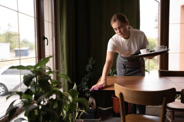 Waiter in cafe cleaning cups and wiping table after customers, hospitality service concept
