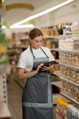 Busy female sales assistant in a grocery typing on the tablet while taking inventory. copy space