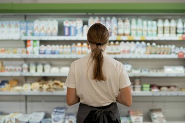 Back view of female staff standing near milk bottles in shelf at dairy section of supermarket. copy space