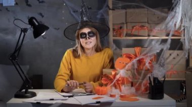 Dropshipping owner in halloween makeup and witch costume takes order online video call. Webcam view. Business woman working in the office. Online marketing. discounts and promotions for Halloween