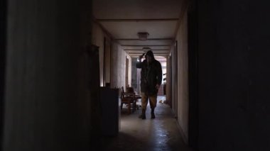 A male researcher in a gas mask with a flashlight inside the corridor of an old ruined room, finds canned food in an old refrigerator. The concept of post-apocalyptic world. Looking for food
