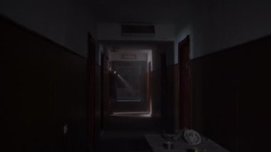 man in clothes with a hood and a gas mask walking along an old abandoned corridor in smoke or fog with a flashlight in his hands. Dystopian concept, future, male survivor. Post-apocalyptic world.