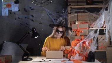 A small business owner prepares a box for Halloween by gluing an address on the packaging while working in a home office. SME, Halloween, shipping concept