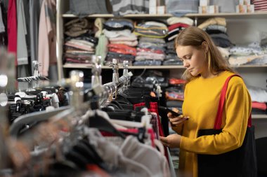 Mağazadan yeni kıyafetler seçen olumlu bir kadın, kıyafet satışından alışveriş yapan genç bir kadın. Alışveriş kıyafetleri moda konsepti
