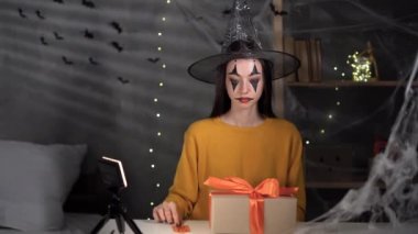 A girl dressed as a witch unpacks a Halloween present while sitting at a table at night. Telemarketing, SME, holiday sale concept