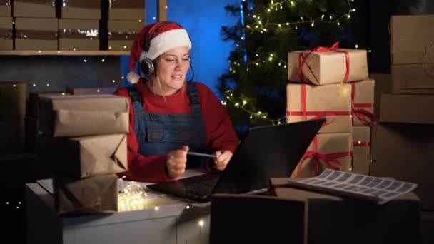 スタートアップ事業 クリスマスの前夜に自宅のオフィスで箱を扱う女性 休日の贈り物の配達とオンライン注文 大きなクリスマスセール — ストック動画