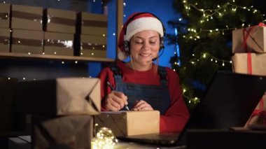concept of small and medium business start-up Caucasian woman in santa claus costume sits in home office at laptop and takes online orders from the site. good earnings during the christmas sale.